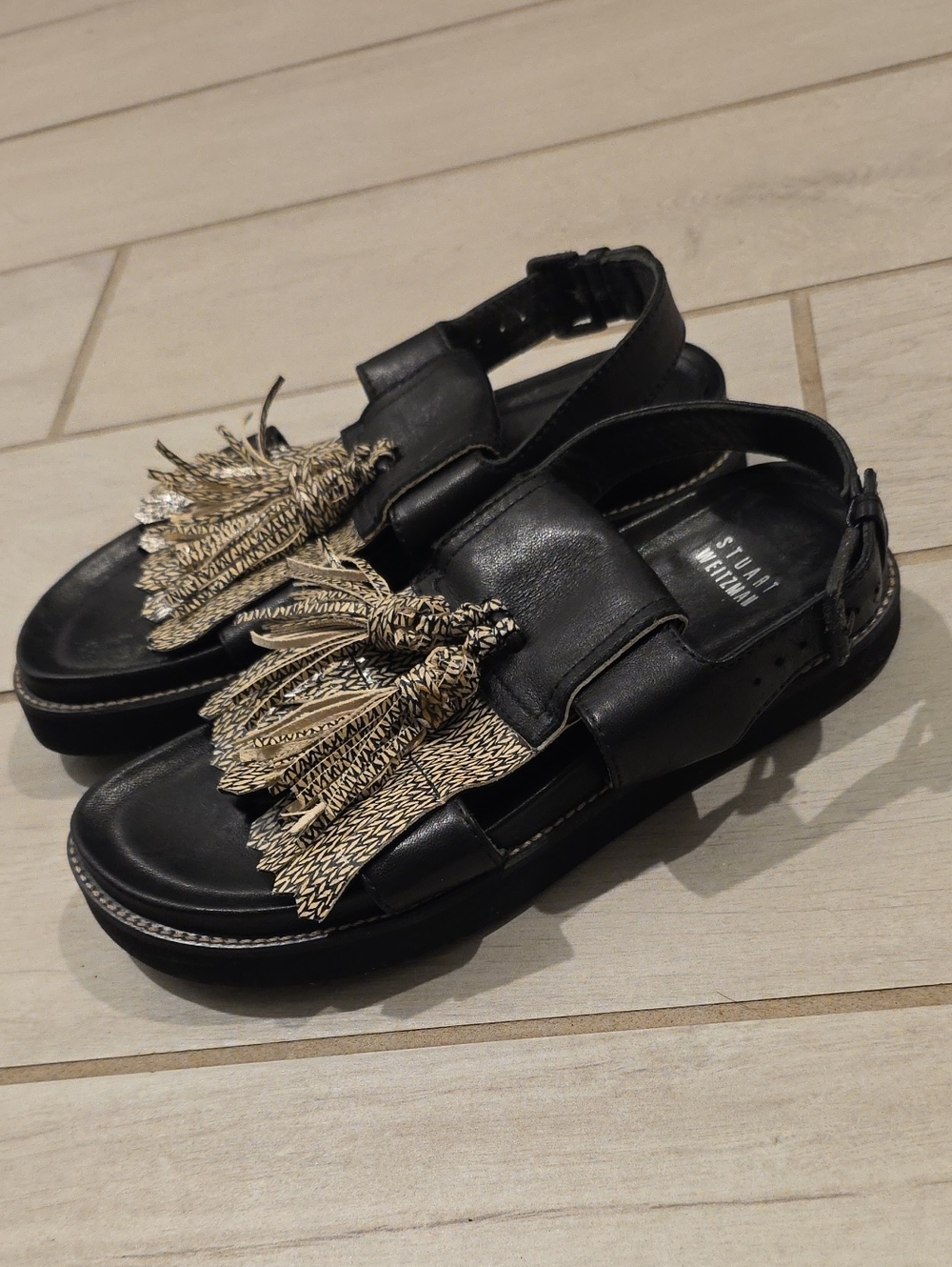 Stuart Weitzman tassel sandals featuring woven metallic detailing.